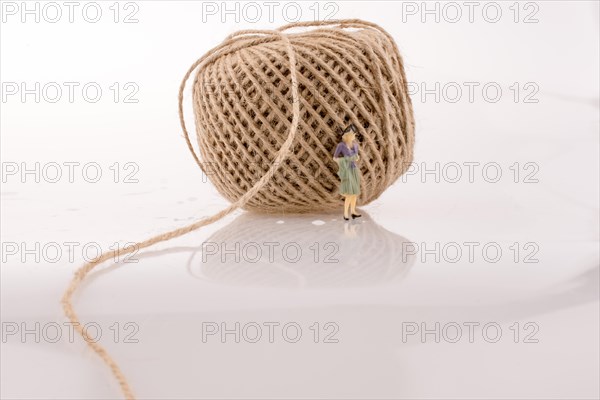 Woman figure beside a linen spool of thread on a white background