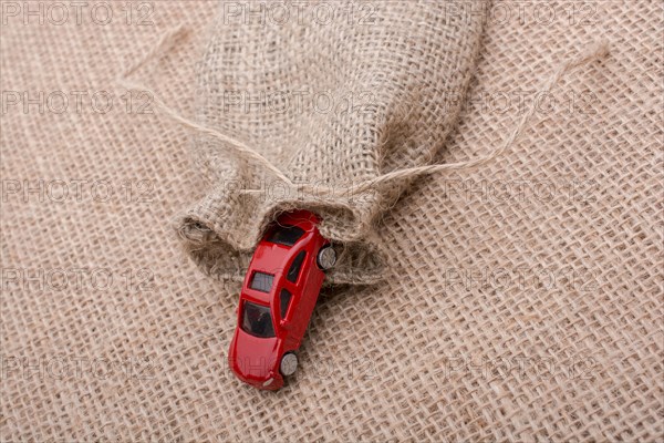 Red toy car coming out of a linen sack on a linen canvas