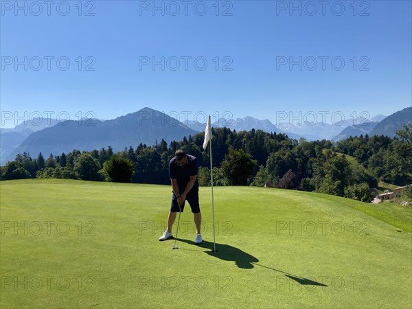 Golfer on Putting Green with Mountain View in a Sunny Summer Day in Burgenstock