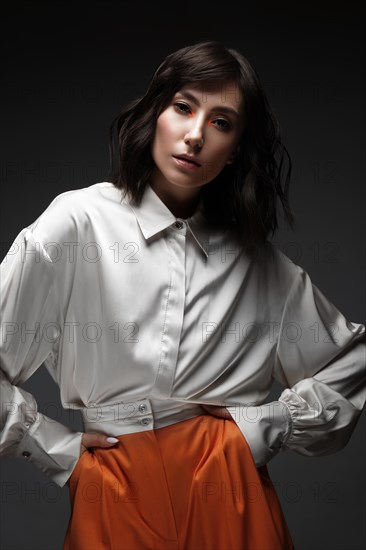 Spectacular beautiful woman in a trendy orange suit with classic make-up. Beauty face. Photo taken in the studio on a white background