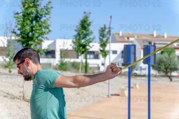 Profile view of a bearded man with sunglasses stretching his back with an elastic strap