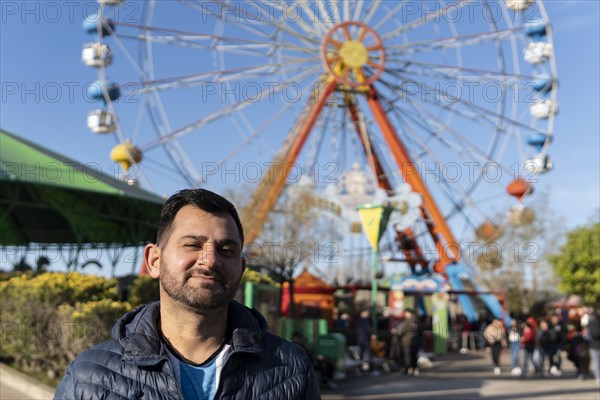 Portrait of latino man in an amusement park posing happy with the ferris wheel in the background