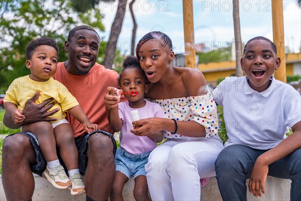 African black ethnic family with children in playground having fun blowing soap bubbles