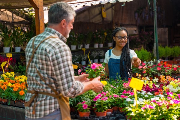 Female customer buying flowers from a gardener in a nursery inside the greenhouse