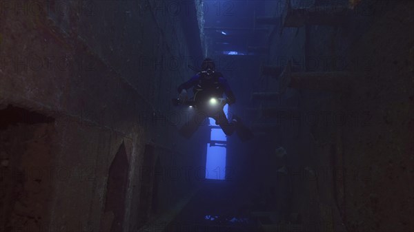 Scuba diver with lantern floats inside of ferry Salem Express shipwreck