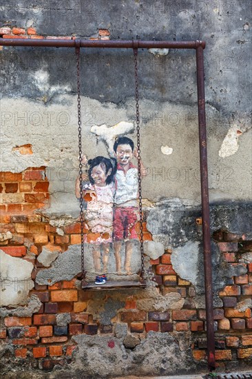 Street art brother and sister on a swing on a wall in George Town on Penang Island