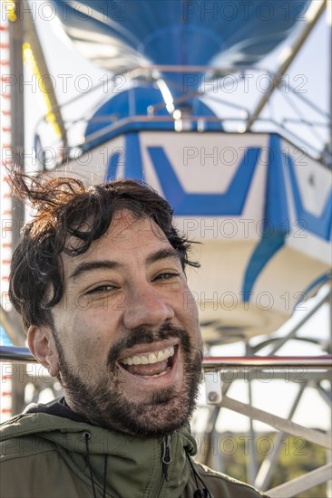 Very excited emotional portrait of a young latin man in the cabin of a ferris wheel. Amusement park adventures and fear of heights