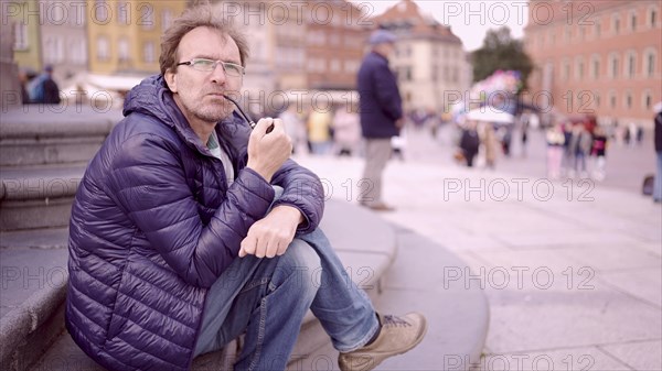 Adult man sitting on square and smoking a tobacco pipe in the Palace Square