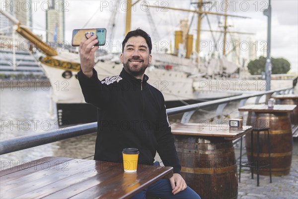 Latin tourist drinking coffee and taking a selfie at an outdoor bar in Puerto Madero