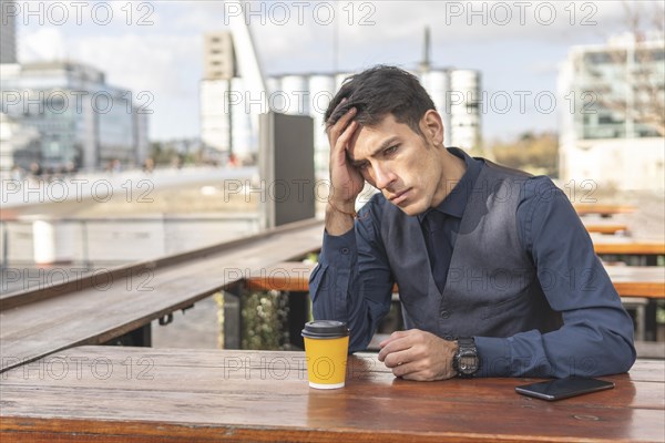 Businessman sitting in an outdoor bar having a coffee clutching his head with a worried expression