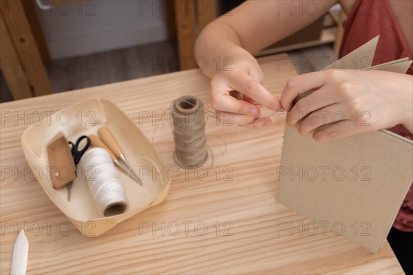 Close-up detail of woman's hands sewing a handmade notebook made in her workshop