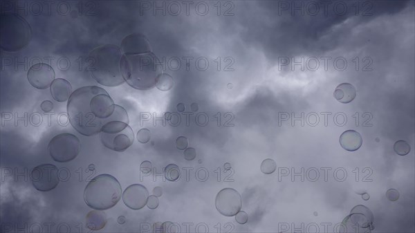Soap bubbles are flying on gray cloudy sky background