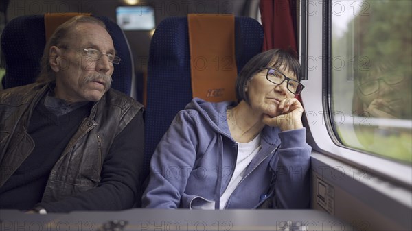 Elderly couple is riding in a train carriage and looking out the window