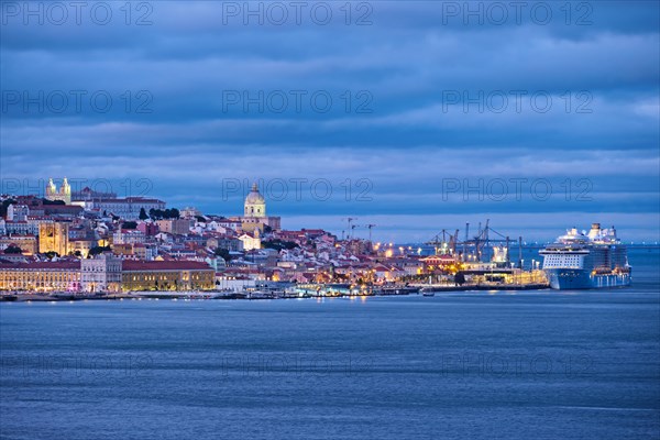 View of Lisbon over Tagus river with passing ferry boat from Almada with moored cruise liner in evening twilight. Lisbon
