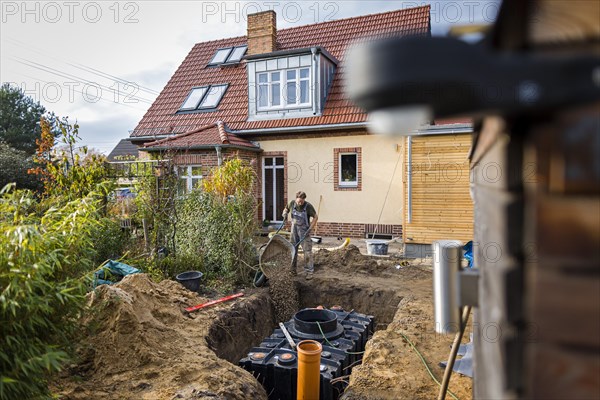 A man installs a water cistern in the garden next to his house to be able to water his garden with rainwater. Berlin