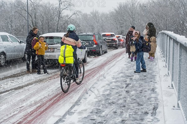 Cyclist and children walking to school over slippery pavement on bridge covered in sleet during unexpected late snow shower in March