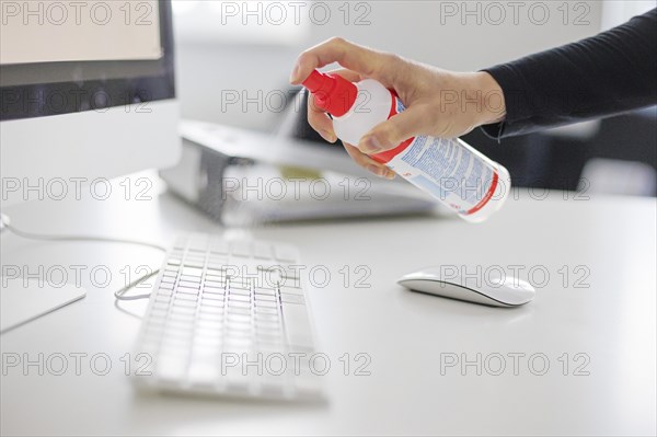 Hygiene at the workplace. A woman disinfects the keyboard at her workplace with disinfectant spray. Berlin