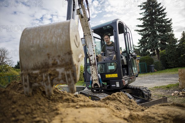 A construction worker sits in a mini-excavator at a building site. Berlin