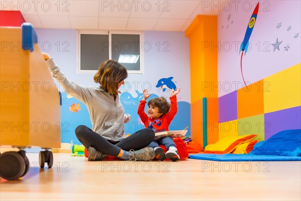 Woman teacher with a child sitting reading a book and laughing with things from the story