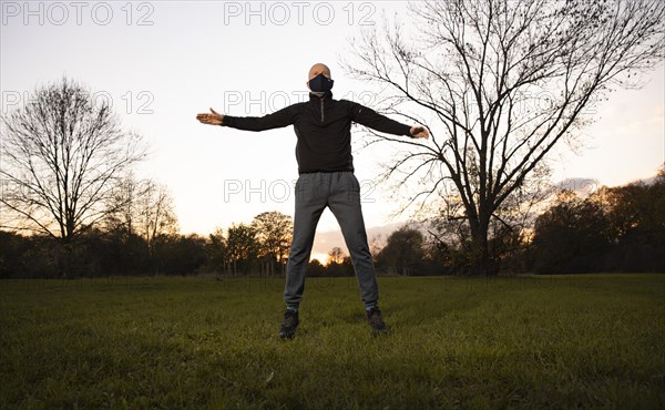 Man with mask stretches in a meadow in autumn.