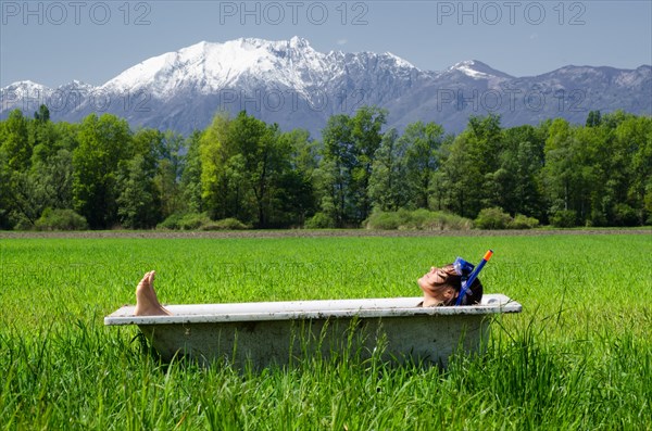 Woman lying in a bathtub on a green field with grass and trees