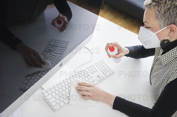 Hygiene at the workplace. A woman disinfects the keyboard at her workplace with disinfectant spray. Berlin