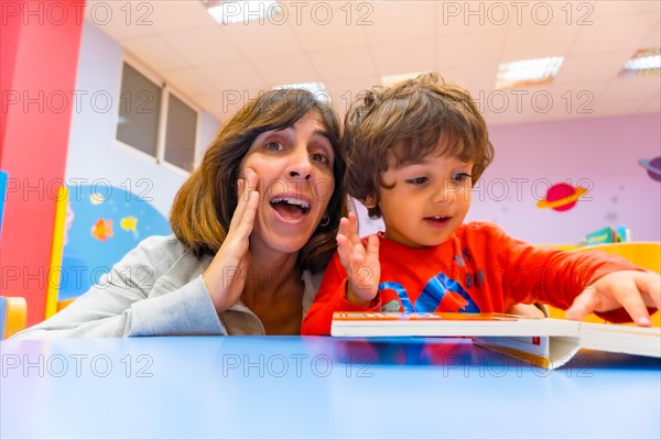 Woman teacher with a child sitting at a table reading a story book