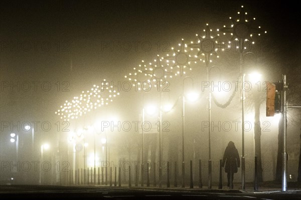 A woman walks along a street decorated with Christmas lights in the fog in Niesky