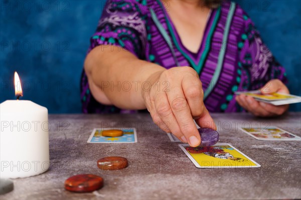 Unrecognizable woman casting tarot cards on the table candles and chakra stones