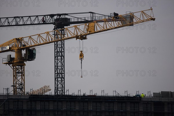 A worker draws on scaffolding and in front of a crane on a newly built house