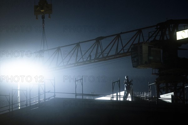 A worker draws on scaffolding and in front of a crane on a newly built house