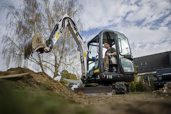 A construction worker sits in a mini-excavator at a building site. Berlin