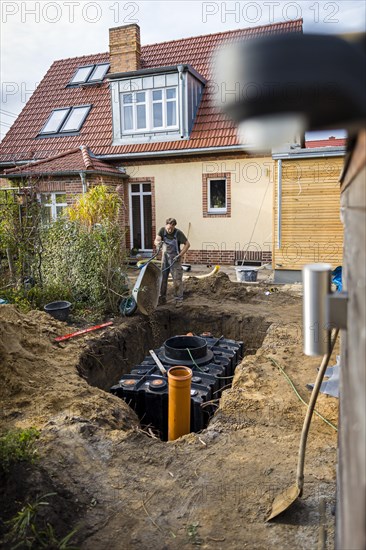 A man installs a water cistern in the garden next to his house to be able to water his garden with rainwater. Berlin