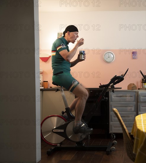 Man on a spinning wheel in his kitchen eating a yoghurt during the Corona Crisis lockdown