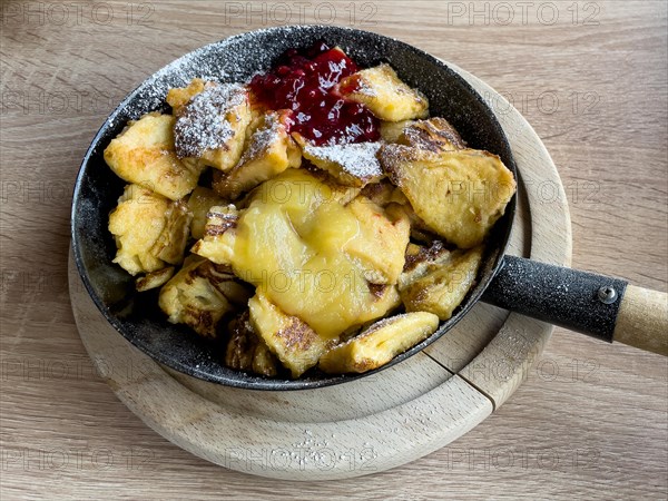 Cast iron frying pan with handle with classic dish from alpine cuisine Kaiserschmarrn sprinkled with icing sugar