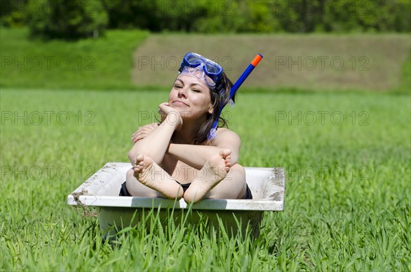 Woman Sitting in a Bathtub on a Green Field with Grass and a Diving Mask in a Sunny Day