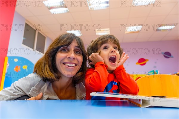 Woman teacher with a child sitting at a table reading a story book