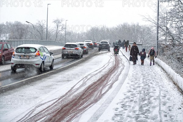 Cars and children walking to school over slippery pavement on bridge covered in sleet during unexpected late snow shower in March 2023