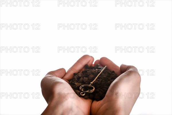 Golden key in handful soil in hand on an isolated background