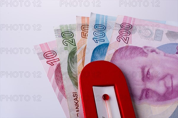 Turkish Lira banknotes by the side of a red color temperature on white background