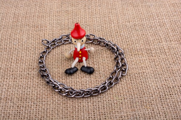 Chain around wooden Pinocchio doll sitting on canvas background