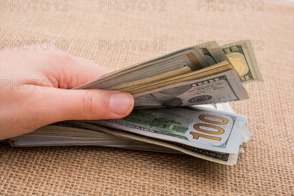 Hand holding banknote bundle of US dollar on a linen canvas background