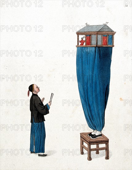 A Chinese puppeteer standing on a stool and balancing a miniature stage above him