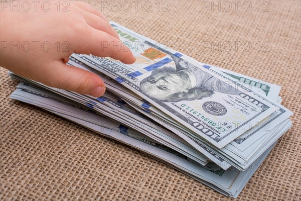 Toddler hand holding banknote bundle of US dollar on a linen canvas background