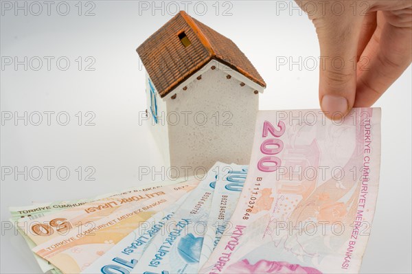 Hand holding Turkish Lira banknotes by the side of a model house on white background