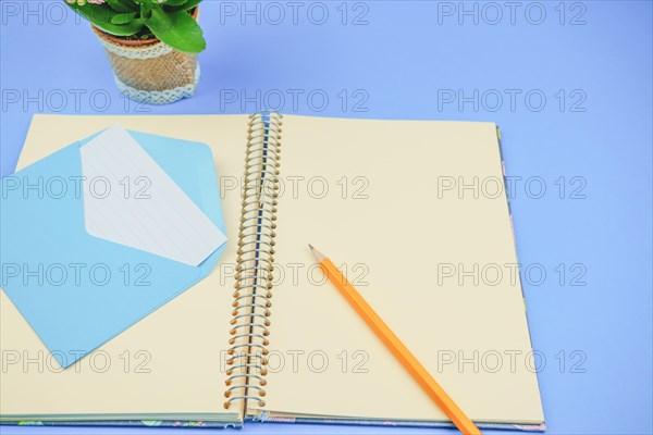 Pencil on a blank notebook with a blue envelope with a letter in it