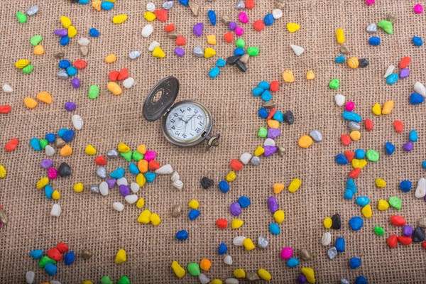 Pocket watch amid colorful pebbles on canvas background