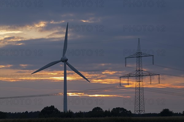 Wind power station and high voltage pylon in front of evening sky