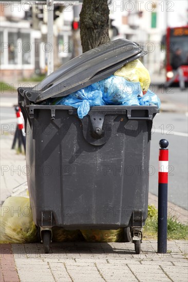 Filled rubbish container with open flap standing by the road