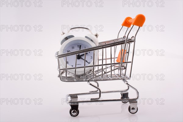 Alarm clock in a shopping trolley on white background